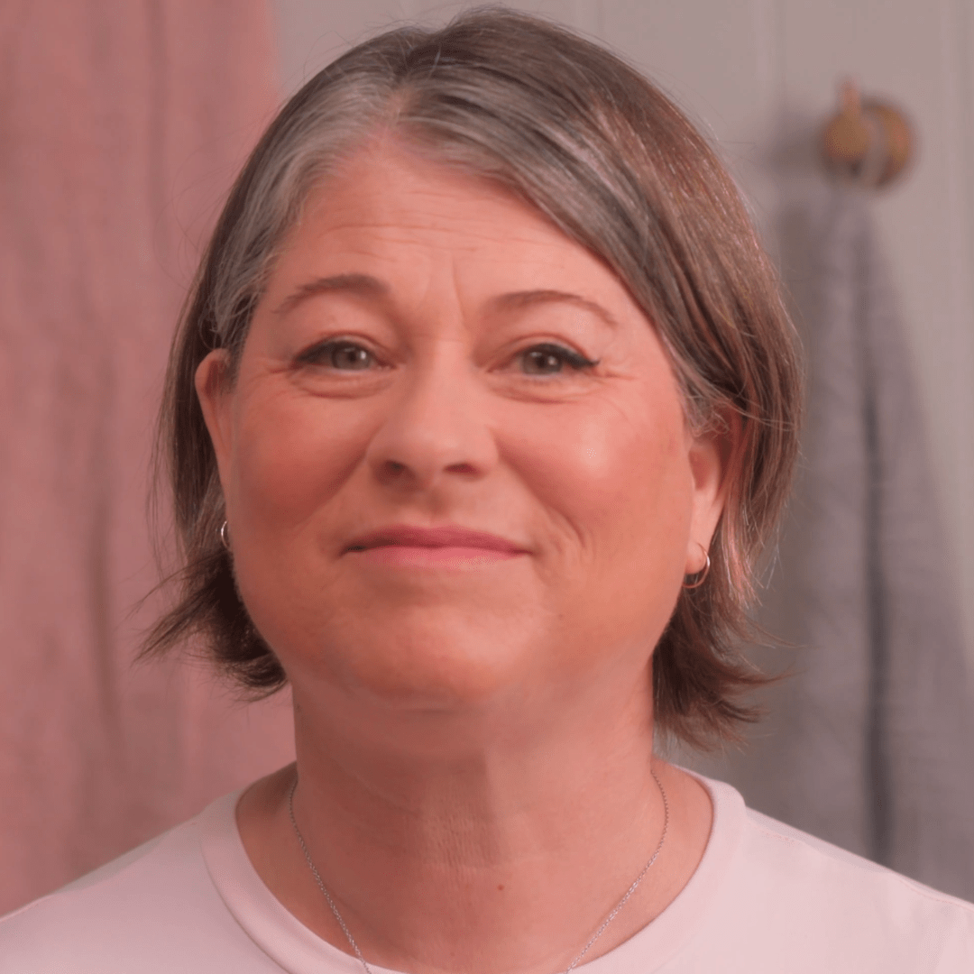 Woman with short gray hair wearing a light pink shirt against a neutral background
