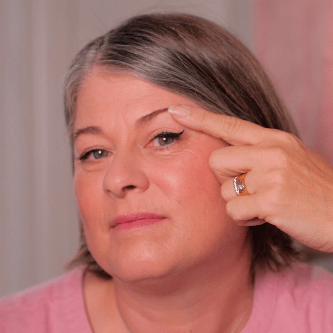 Woman applying makeup to her eye with a neutral background